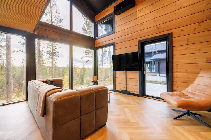 Leather sofa and swivel chair in a corner of windows opening onto pine forest