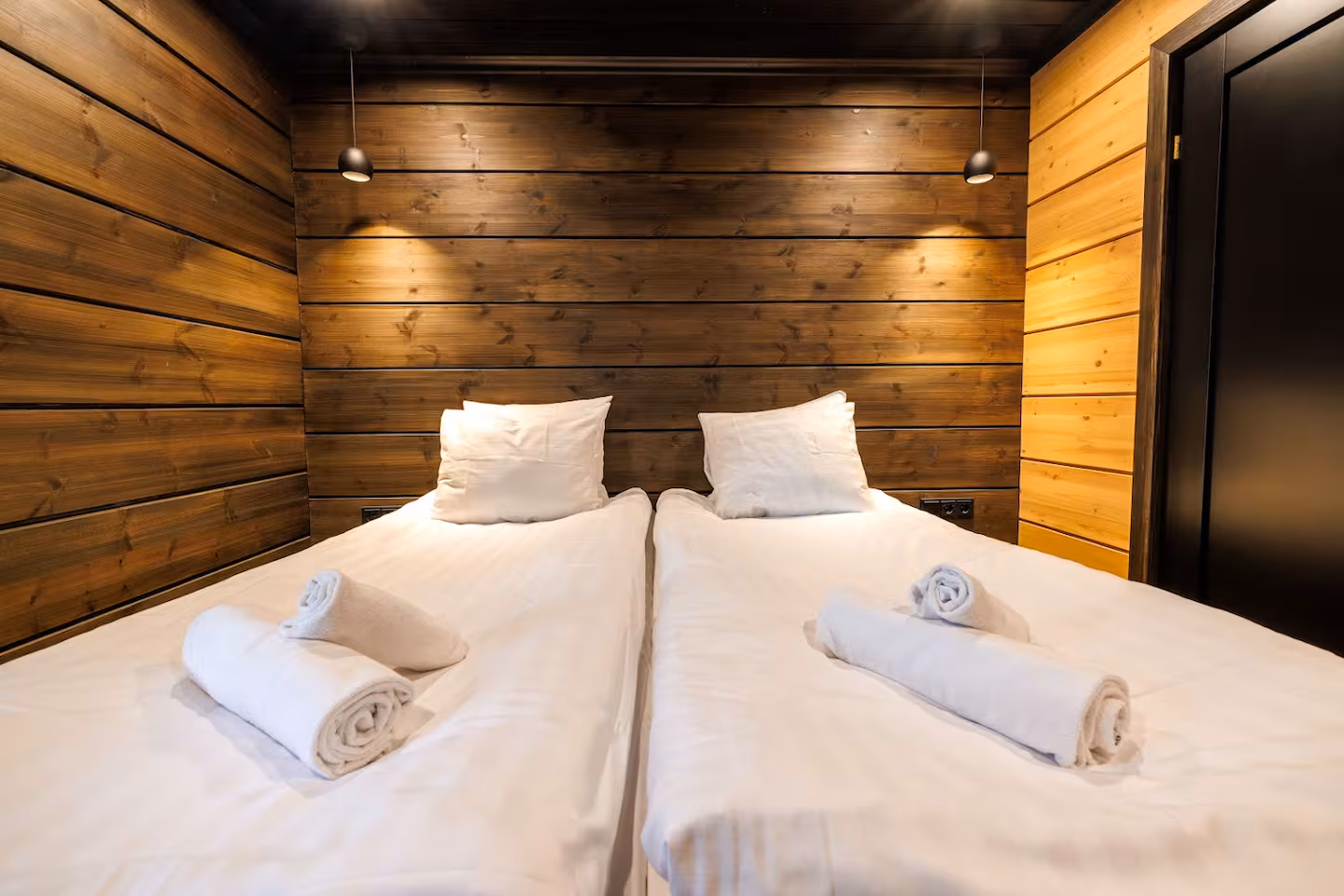 Twin beds against a warm timber wall with reading lights above