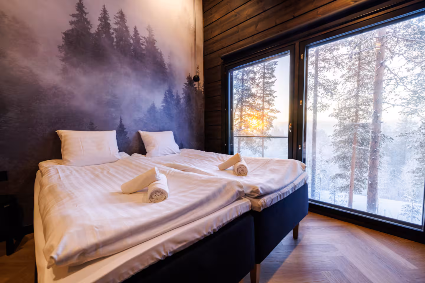 Twin beds made up with white linen against a misty forest mural, sunset through the window