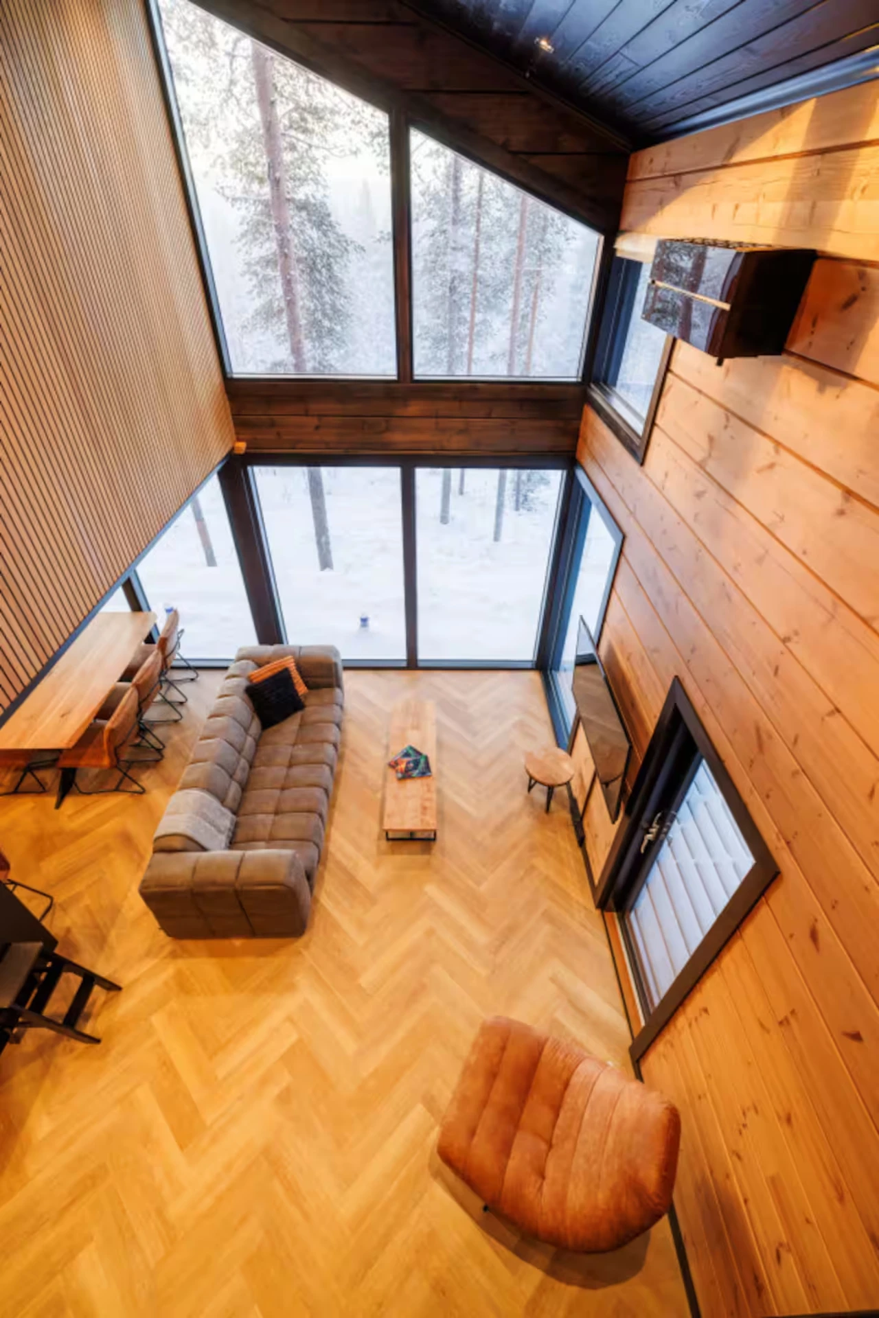 View from the upstairs landing down into the herringbone-floored lounge with full-height forest windows