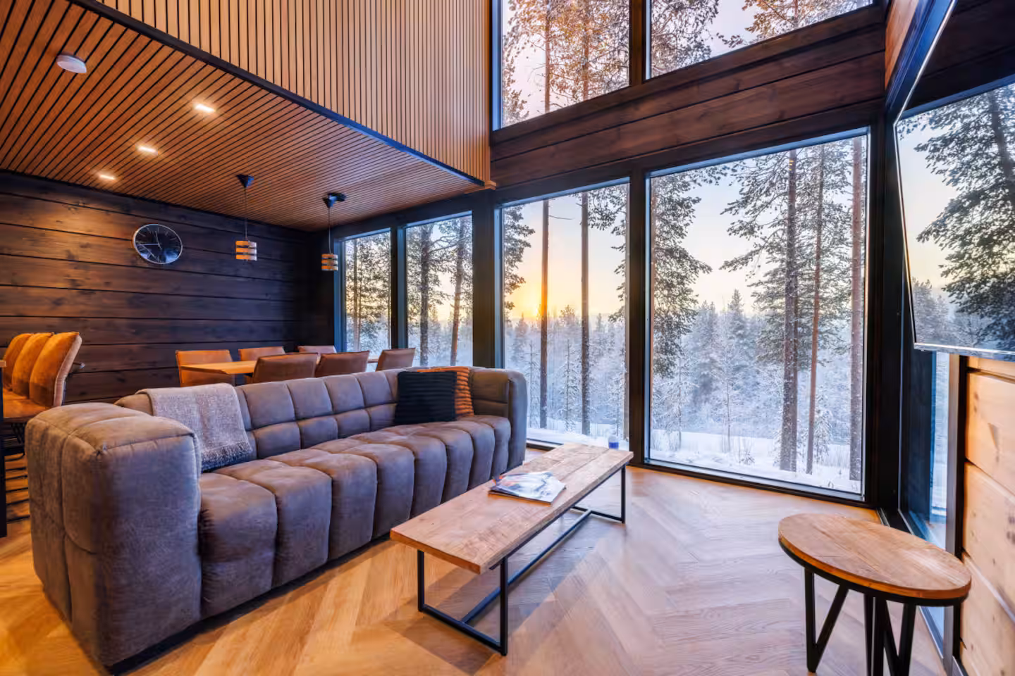 Living room at Villa Kaski with a full-height glass wall onto sunlit pine forest