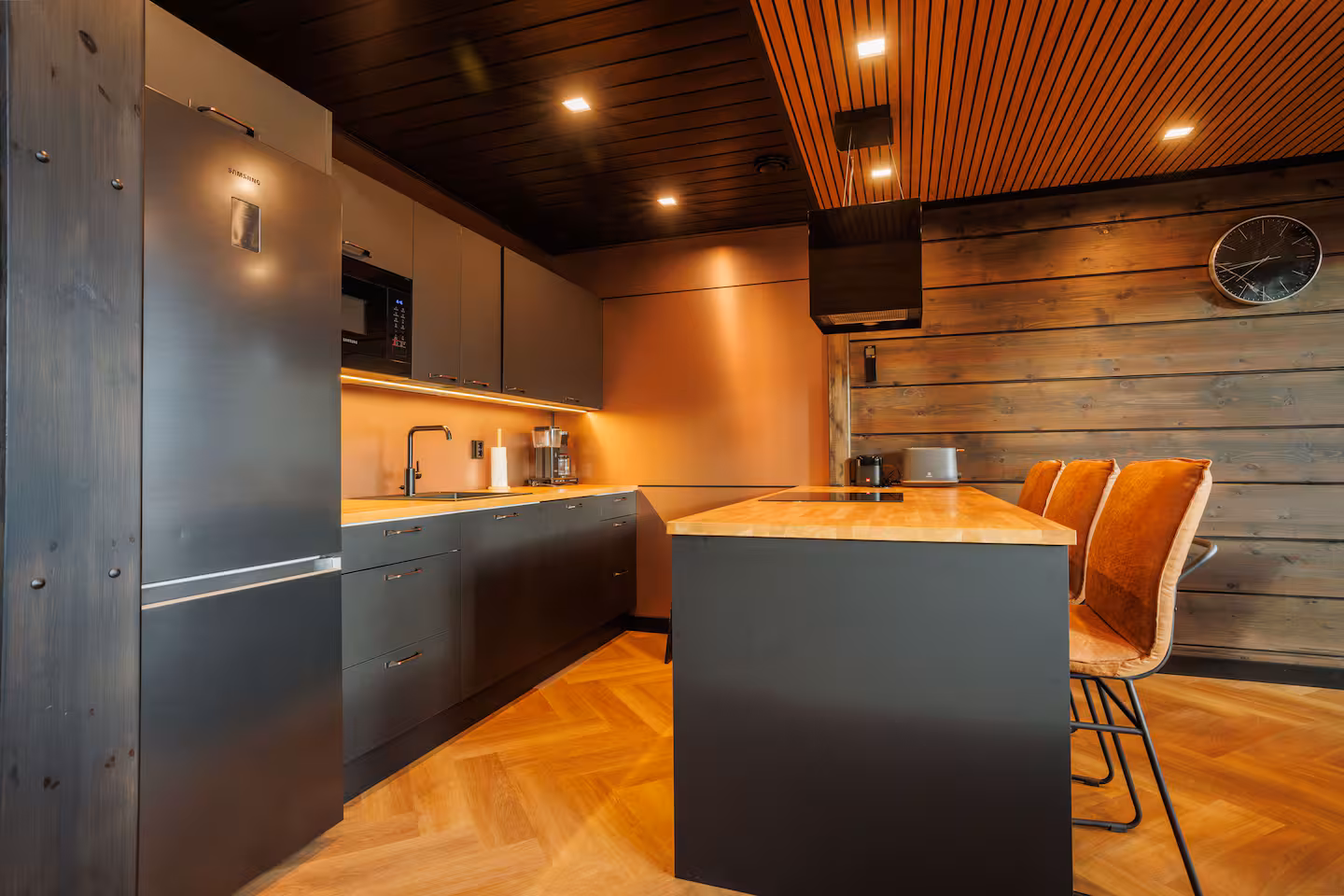 Dark kitchen with an oak-topped island and bar stools under a slatted ceiling