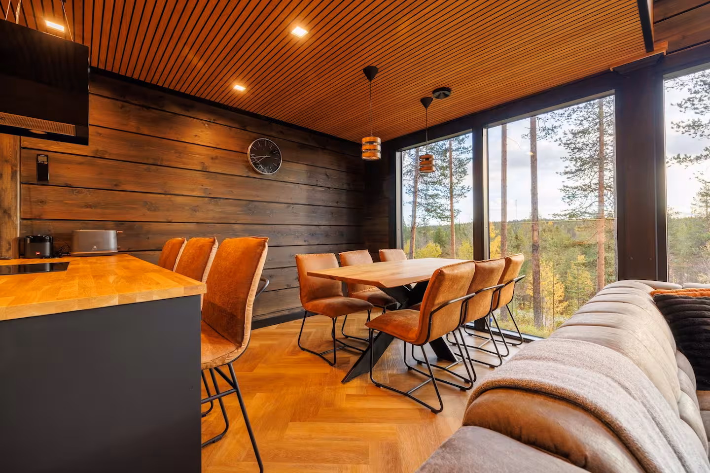 Dining table with tan leather chairs beside the kitchen counter and windows onto autumn forest