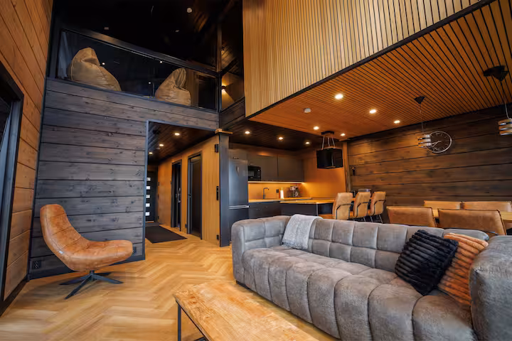Open living room with a large grey sofa, leather swivel chair and a slatted mezzanine above