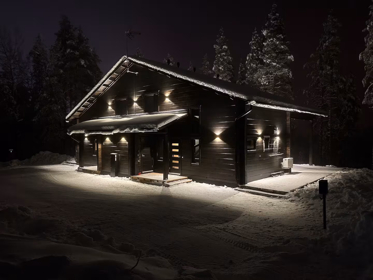 The dark timber villa lit by facade lighting on a snowy winter night