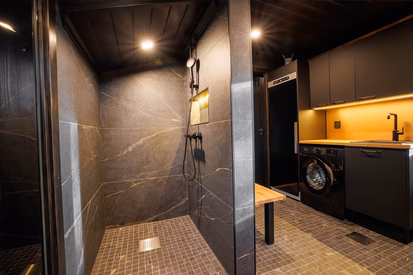 Stone-clad walk-in shower next to a utility area with washing machine and dryer