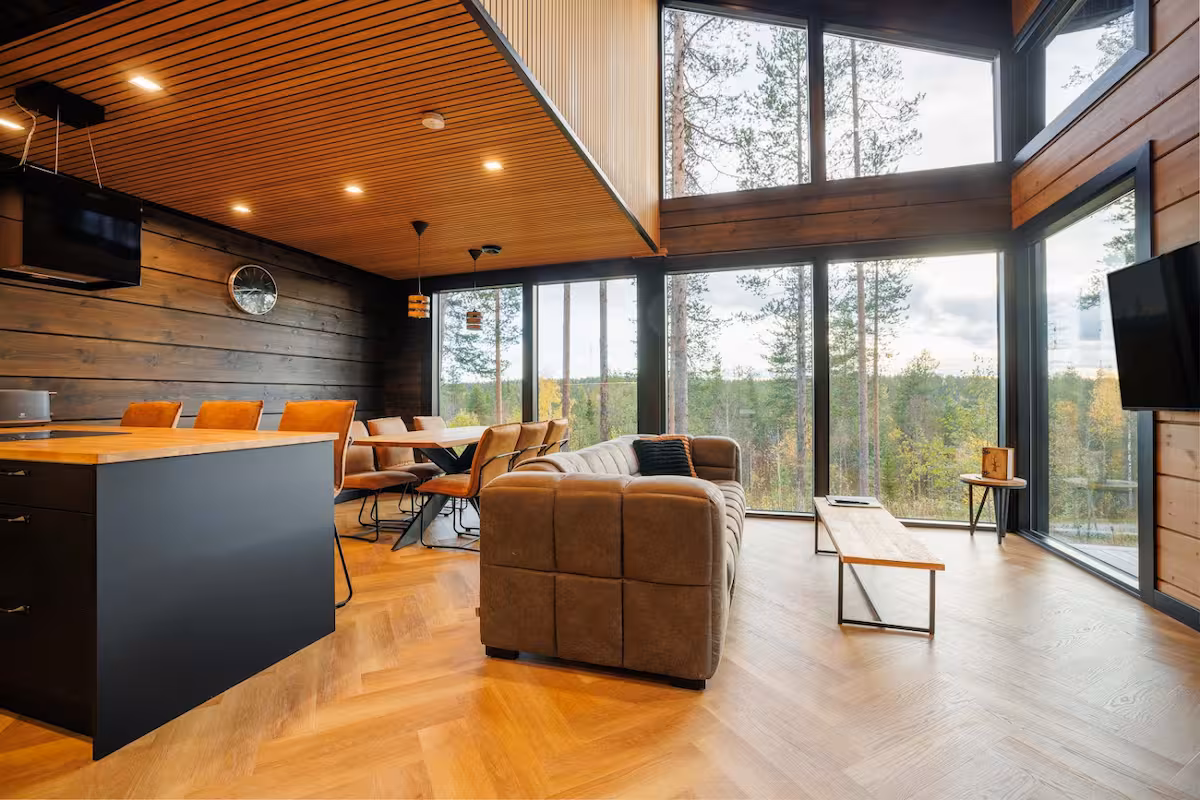 Living and dining space opening through a full-height glass wall onto pine forest