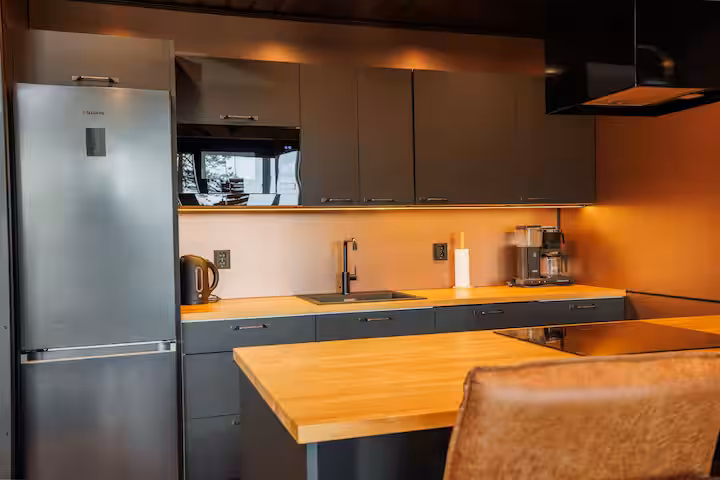 Dark kitchen units with warm under-cabinet lighting and a solid timber worktop
