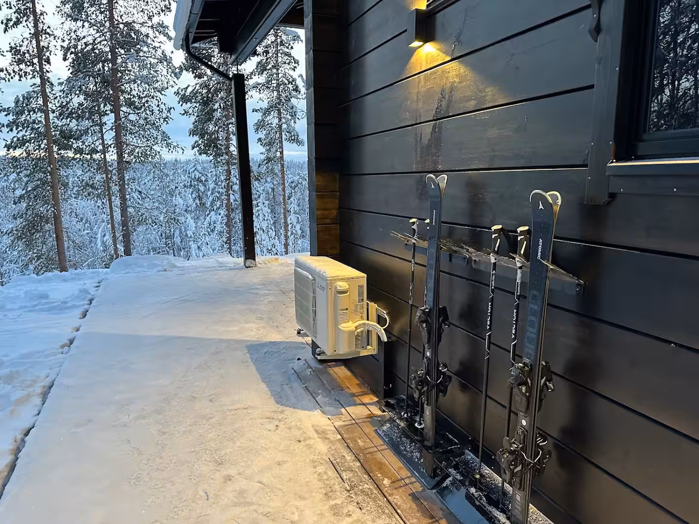 Skis and poles in wall racks beside the entrance, snowy fell view beyond
