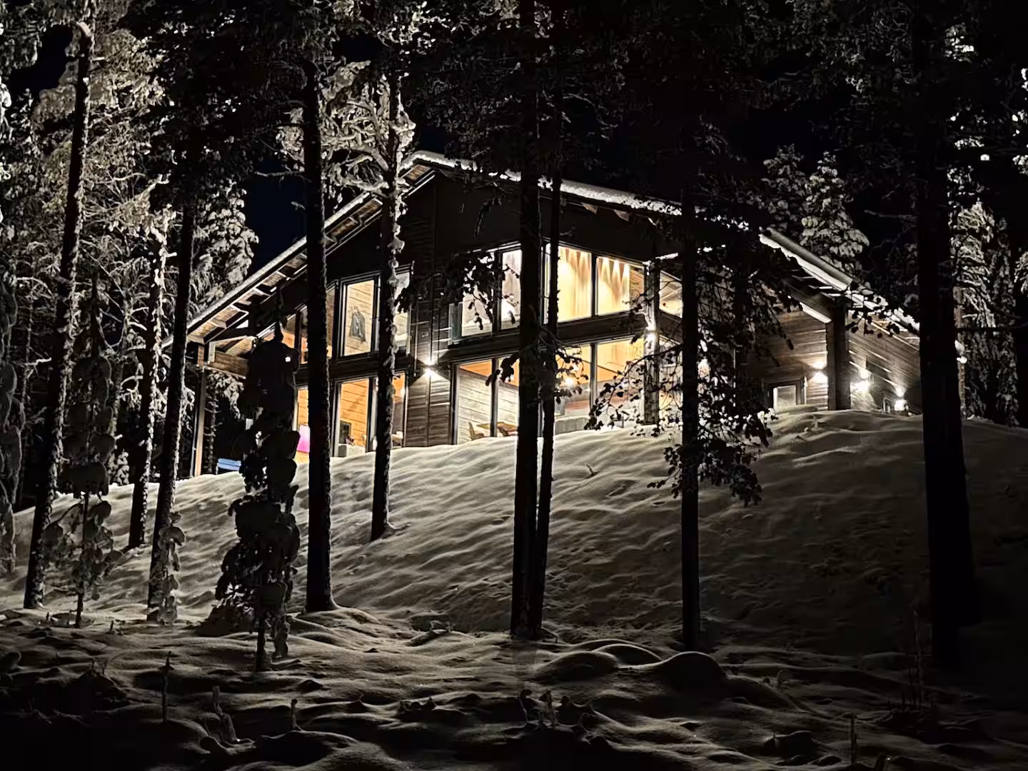 Villa Kaski lit from within at dusk, seen through snow-covered spruce trees