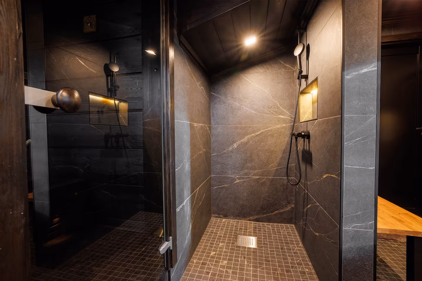 Dark stone-clad shower room with twin showers next to the sauna